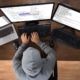 Hooded Hacker Using Three Computers