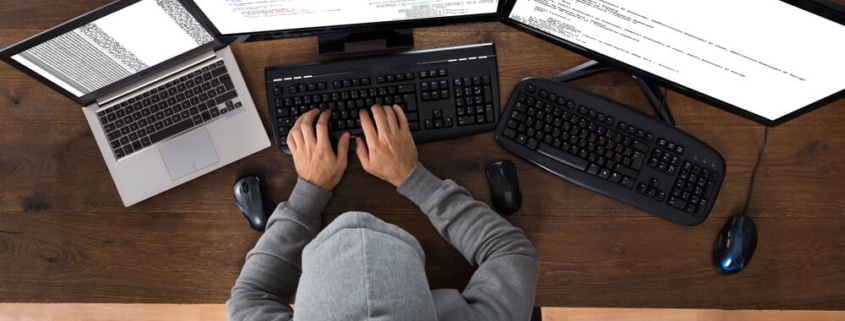 Hooded Hacker Using Three Computers