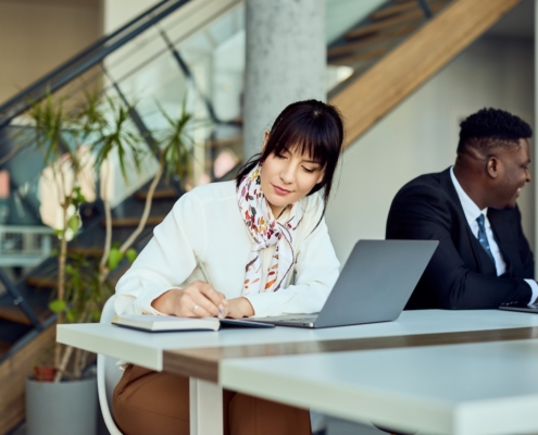 woman working in office writing something in notebook with her laptop on desk